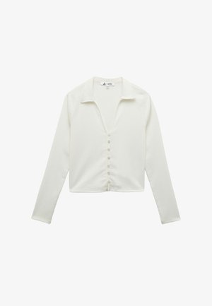 Chemisier blanc à manches longues avec un col, fabriqué en tissu texturé. Il présente un col en V et sept boutons sur le devant.