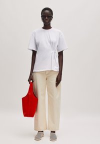 Witte kortelange t-shirt met een strik in de taille, beige wijde broek, rode schoudertas en zwart-wit gestreepte schoenen.