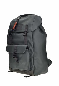 Mochila de color verde oscuro hecha de tela texturizada. Presenta un cierre de solapa, un bolsillo frontal con hebilla y una etiqueta de marca. Los acentos incluyen correas negras.