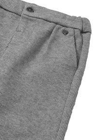 Szare spodnie z teksturowanym wzorem w kratkę, z dwoma czarnymi guzikami w okolicy pasa oraz kieszeniami bocznymi.