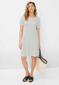 Robe à manches courtes rayée en blanc et noir, présentant une coupe décontractée et un col rond. Associée à un sac en paille tissé et des sandales noires.