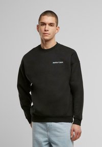 Sudadera de algodón negra con cuello redondo y puños de canalé. Logo bordado "Another Cotton" en azul en el pecho. Corte casual.