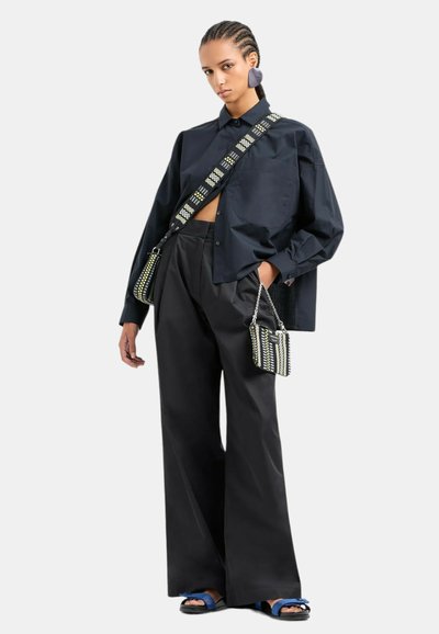 Camicia nera oversize, pantaloni neri a gamba larga, sandali blu e borse con motivi geometrici nei colori nero, bianco e accenti gialli.
