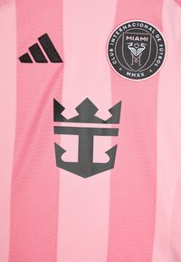 Maglia da calcio rosa con accenti neri. Presenta righe verticali, logo Adidas e un emblema centrale a forma di corona con design a ancora.