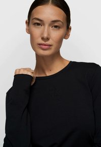 Camiseta negra de manga larga con cuello redondo y logo bordado tono sobre tono en el pecho, confeccionada con una tela suave y elástica.