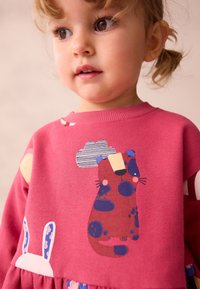 Lyserød sweatshirt med lange ærmer, der har en legesyg kattegrafik, sky og kaninaccents i levende farver, lavet af blødt bomuldsstof.