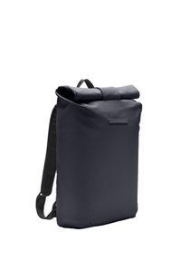 Sac à dos à rabat en bleu marine foncé, fabriqué en tissu durable, présentant une forme élégante et un design minimaliste avec des bretelles réglables et un détail logo subtil.