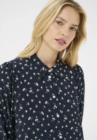 Blomstret skjorte i marineblå stof med hvidt blomsterprint, med klassisk krave og lange, puffede ærmer.