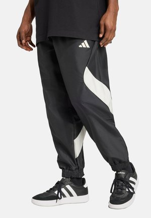 Sorte atletiske bukser lavet af glat stof, med hvide sidedele og en elastisk talje. Båret med sorte sneakers og sokker.