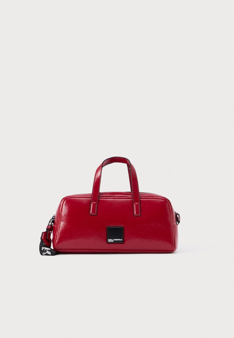 Malá obdĺžniková lesklá červená kabelka s dvoma rúčkami, čiernym zipsom, čiernou nášivkou s logom a odnímateľným čiernym remienkom s bielym textom.