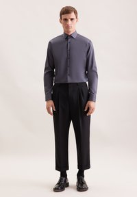 Langarm, charcoal grijze blouse van gladde stof, gecombineerd met zwarte geplooide broek en zwarte veterschoenen.