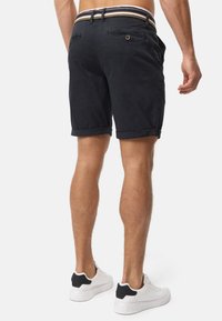 Shorts navy avec un ourlet replié, deux poches arrière et une ceinture à rayures multicolores. Associés à des baskets blanches.