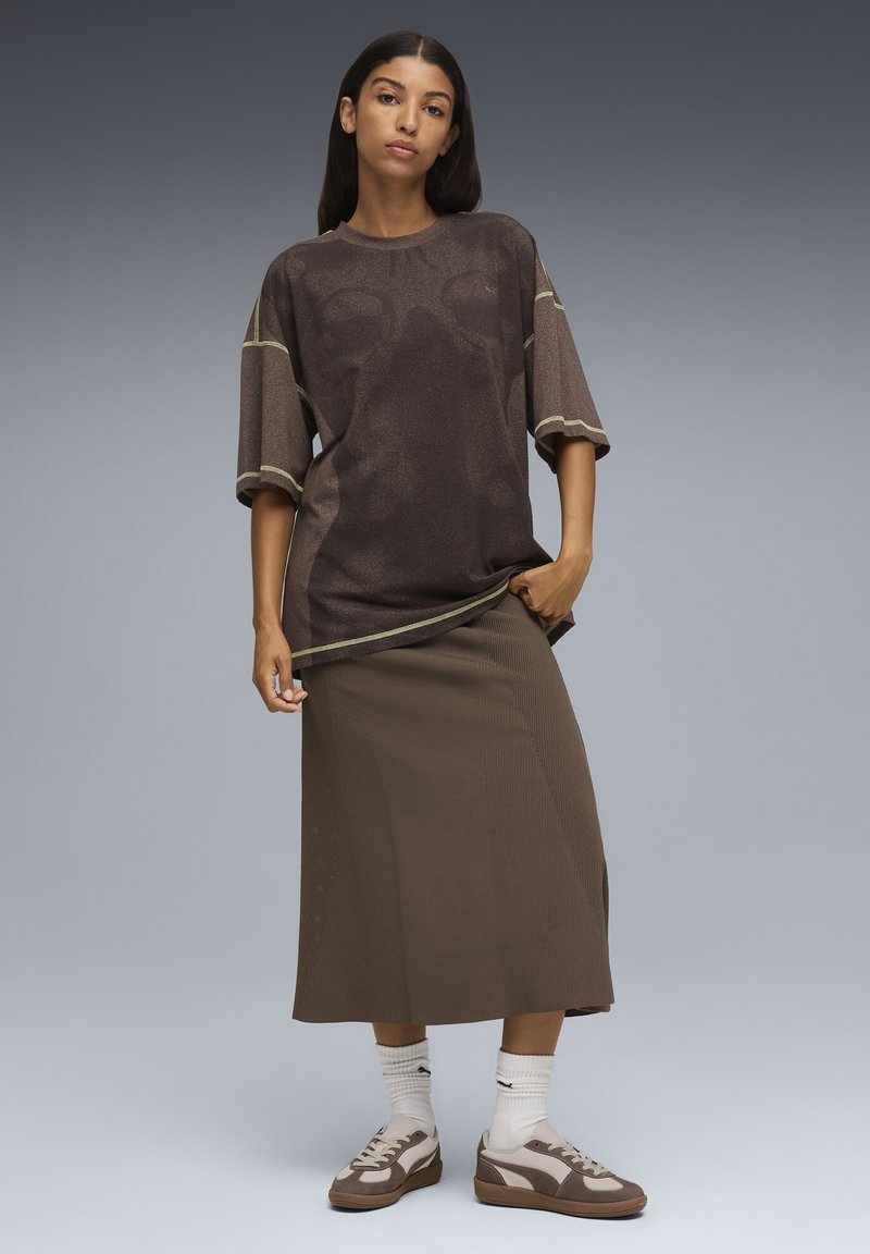 Camiseta marrón oversized con mangas cortas y ribete verde, combinada con una falda de punto marrón. Zapatillas marrón y crema con calcetines blancos complementan el look.