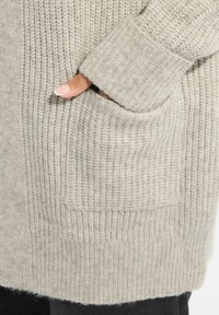 Ljusgrå stickad kofta med ribbat mönster, med en framficka och manschetter på ärmarna. Mjuk och varm material.