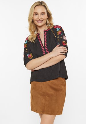 Black textured top with colorful floral embroidery, pink scalloped neckline; paired with a brown suede mini skirt.