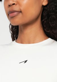 Valge puuvillane T-särk klassikalise lõikega, millel on väikene must logo ülemisel vasakul küljel. Sile puuvillane tekstuur.