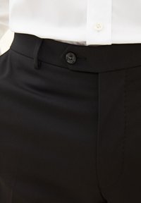 Pantaloni neri su misura con una texture liscia, dotati di chiusura con bottone e passanti per cintura. Cuciture ben rifinite e vestibilità classica.