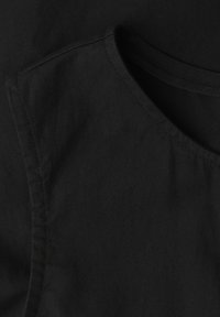 Gros plan sur une chemise en tissu noir montrant un col rond et des coutures détaillées le long de l'épaule et du col.
