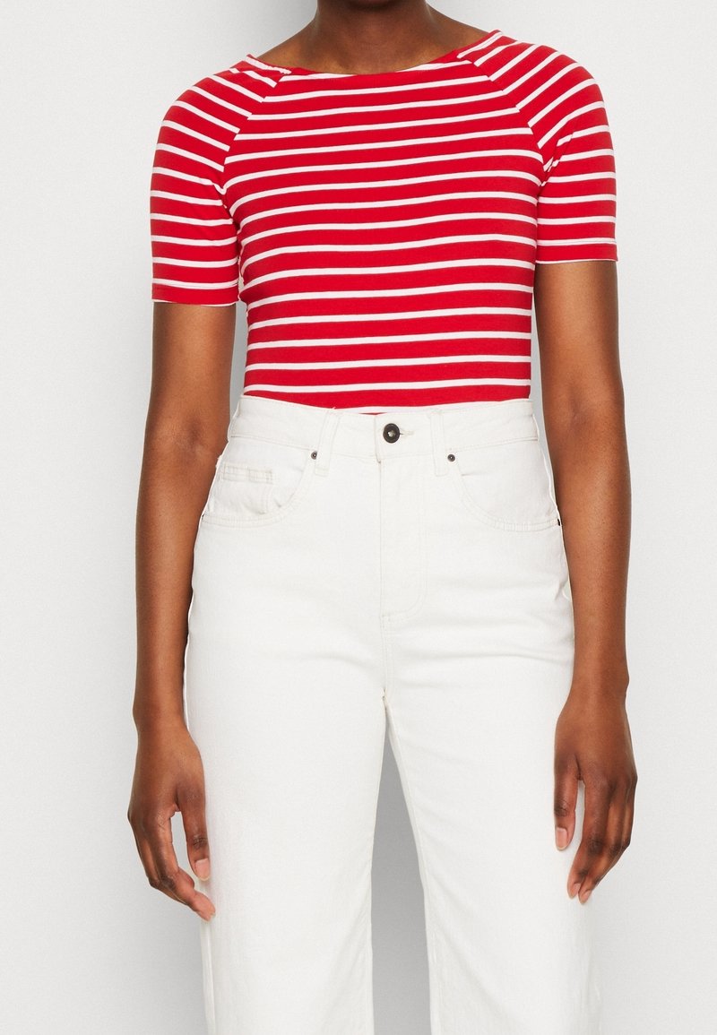 Haut à manches courtes rayé rouge et blanc avec un col bateau, associé à un pantalon en denim blanc taille haute. Tissu doux avec une texture subtile.