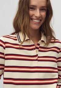 Korte mouwen polo shirt met crème stof en horizontale rode, oranje en donkerpaarse strepen, een kraag en een placket met twee knopen.