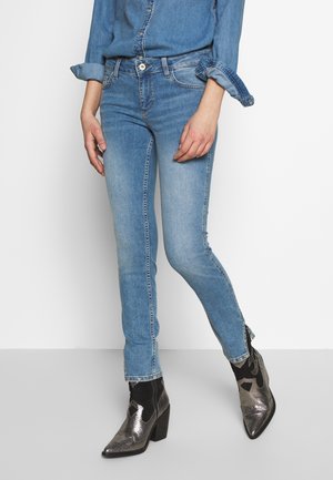 Personne portant un jean skinny bleu clair et des bottines argentées métalliques avec des panneaux élastiques noirs sur les côtés.