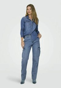 Jeanshemd mit Knöpfen, großen Brusttaschen und langen Ärmeln, kombiniert mit hellblauen Cargo-Hosen mit Seiten Taschen und einer lockeren Passform.