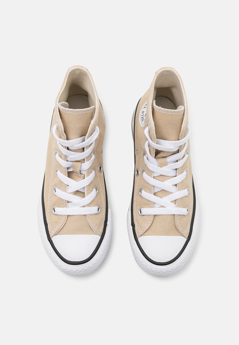 Zapatillas altas de lona beige con cordones blancos, suelas de goma negras y una puntera blanca. Presentan un parche de logo redondo en el lateral.