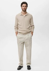 Suéter de punto beige con cuello, combinado con pantalones plisados beige claros y mocasines negros. Texturas suaves y colores neutros.
