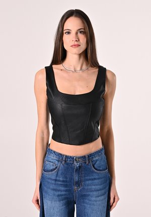 Top corto in pelle nera con scollatura quadrata e design aderente, abbinato a jeans azzurri chiari con vestibilità rilassata. Dettagli in argento per il collier.
