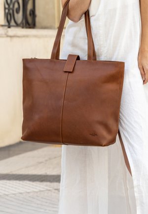 Bruine leren tote bag met een gladde textuur, rechthoekige vorm, ritssluiting en twee stevige handvatten. Subtiele stiksels zichtbaar.