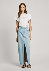 Bílá tričko s potiskem "Pepe Jeans", doplněné dlouhou světle modrou džínovou sukní s předním rozparkem a černými sandály.