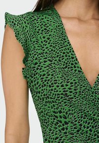 Robe verte avec un imprimé léopard noir et blanc, présentant un décolleté en V profond et des manches courtes à volants sur le haut du torse d'une femme.