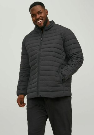 Chaqueta de abrigo negra con acolchado horizontal, cuello alto y cierre frontal de cremallera. Cuenta con bolsillos laterales y una textura suave y mate.