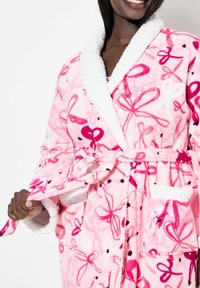 Růžový flísový župan s bílým límcem ze sherpy. Vzorovaný růžovými mašlemi a tečkami, se zavazovacím pasem a předními kapsami. Měkká textura.