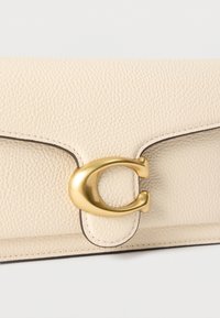 Πορτοφόλι από δέρμα με κρεμ υφή και χρυσό μεταλλικό κούμπωμα σε σχήμα γράμματος C σε λευκό φόντο.