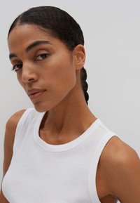 Top in cotone bianco a costine con scollatura rotonda e design senza maniche, caratterizzato da una texture liscia e una silhouette aderente.