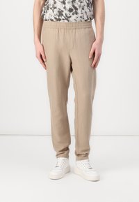 Beige, elastische Hosen mit geradem Bein aus leichtem Material. Kombiniert mit weißen Turnschuhen. Minimalistischer Stil.