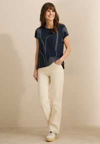 Námořnické tričko s krátkým rukávem a bílými pruhy, v kombinaci s béžovými kalhotami s vysokým pasem a krémovými teniskami. Minimalistický a ležérní design.