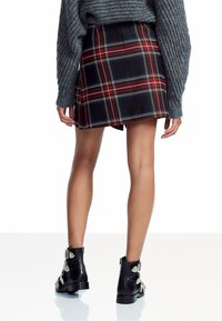 Zwarte en rode geblokte mini rok met plooien, gecombineerd met een grijze textuurtrui en zwarte enkellaarsjes met decoratieve hardware.
