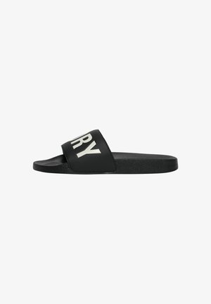 Schwarze Slide-Sandale mit einem breiten Riemen oben, auf dem in Weiß die Buchstaben „RY“ zu sehen sind.
