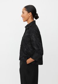 Sort jakke med et tekstureret blomsterdesign, cropped silhuet og trekvartærmer. Har krave og lukning med knapper fortil.
