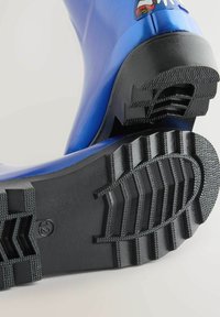 Stivale di gomma blu con una suola nera testurizzata, caratterizzato da un motivo di battistrada per una migliore aderenza. Include una distintivo decorativo di un personaggio sul lato.