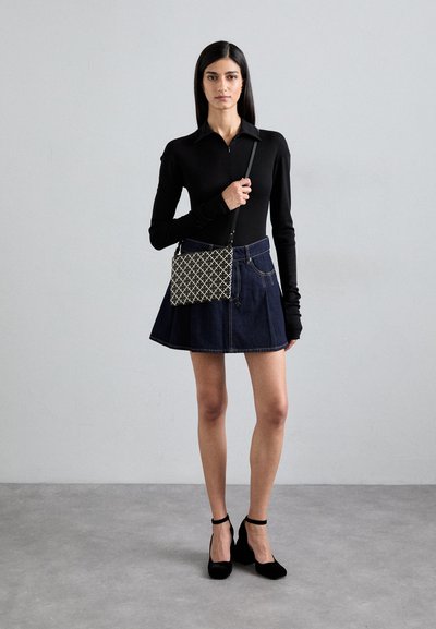 Top nero a maniche lunghe, gonna in denim a campana e scarpe con tacco alte nere. Una borsa a tracolla con pattern è tenuta di lato. Sfondo semplice.