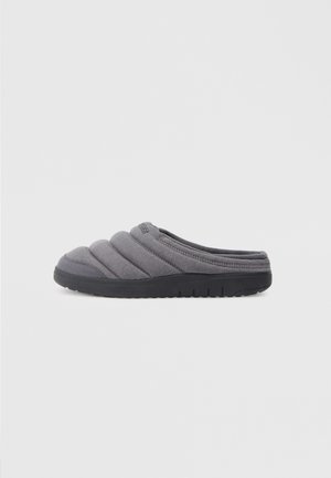 Šedá nazouvací bota s polstrovaným svrškem, který má prošívaný design, a černou gumovou podrážku. Lehká konstrukce, vhodná pro použití uvnitř.