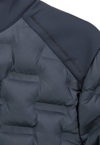 Dunkelgrauer gesteppter Stoff mit dicken gepolsterten Abschnitten und einem schwarzen gestickten Etikett mit der Aufschrift "Atlantic Urban Explorer / Dev. 1X" im oberen Teil.