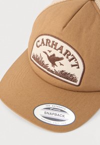 Καπέλο snapback σε ταμπά χρώμα με επιγραφή Carhartt που απεικονίζει πουλί σε πτήση και κέντημα με χόρτα στο μπροστινό πάνελ.