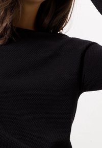 Zwarte gebreide trui met een ronde halslijn en lange mouwen. De stof heeft een verhoogd patroon, wat een subtiele tactiele kwaliteit biedt.