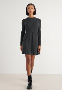 Robe en tricot gris charbon avec texture côtelée, manches longues, col rond et jupe évasée. Tissu lisse avec une finition douce.