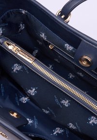 Wnętrze granatowej skórzanej torebki prezentujące złoty zamek błyskawiczny, materiałowe wykończenie z powtarzającym się jasnoniebieskim wzorem logo oraz liczne przegródki.