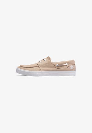 Chaussure bateau en toile beige avec semelle en caoutchouc blanche, lacets blancs et détails cousus, avec un petit logo arbre blanc près du talon.